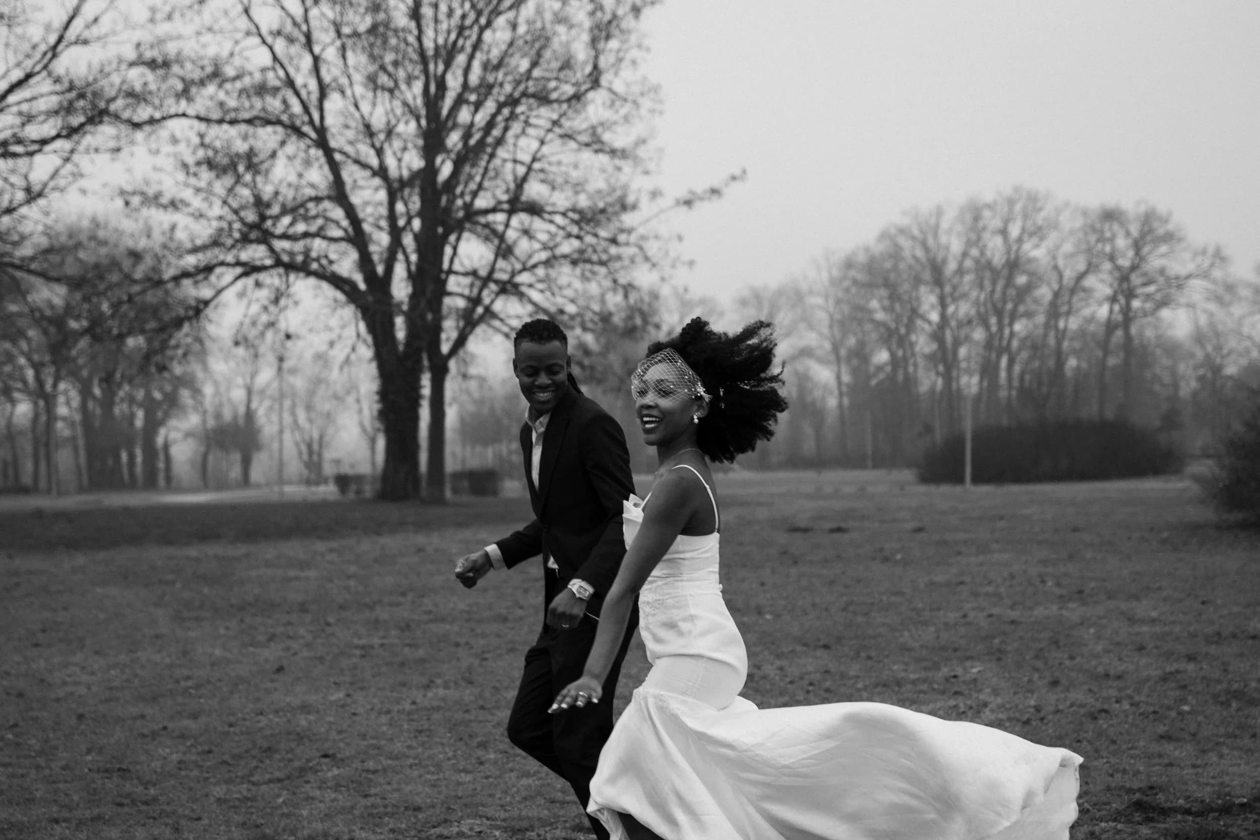 Bride and groom laughing, running together across a park